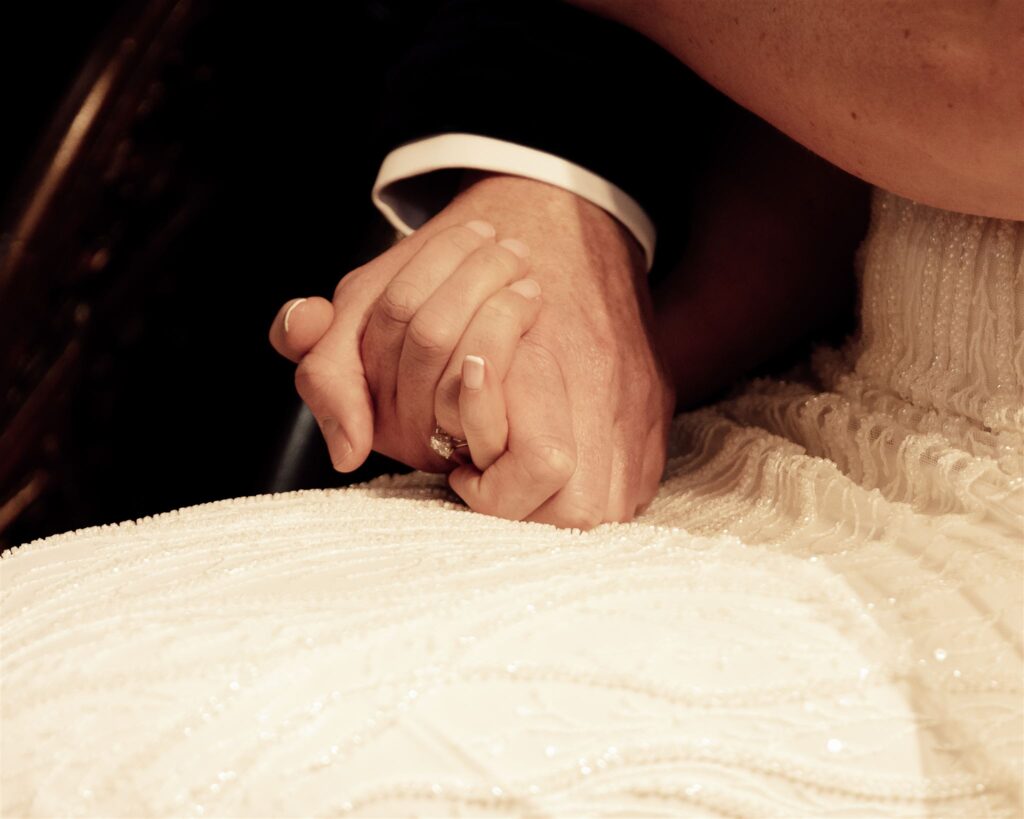 Holding each others hands during a wedding service. The photo shows just their hands.