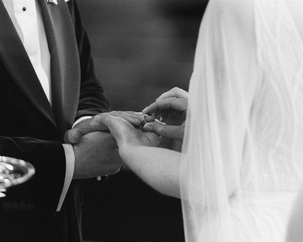 A ring exchange. The bride places the wedding ring on the groom. The photo shows just their hands.